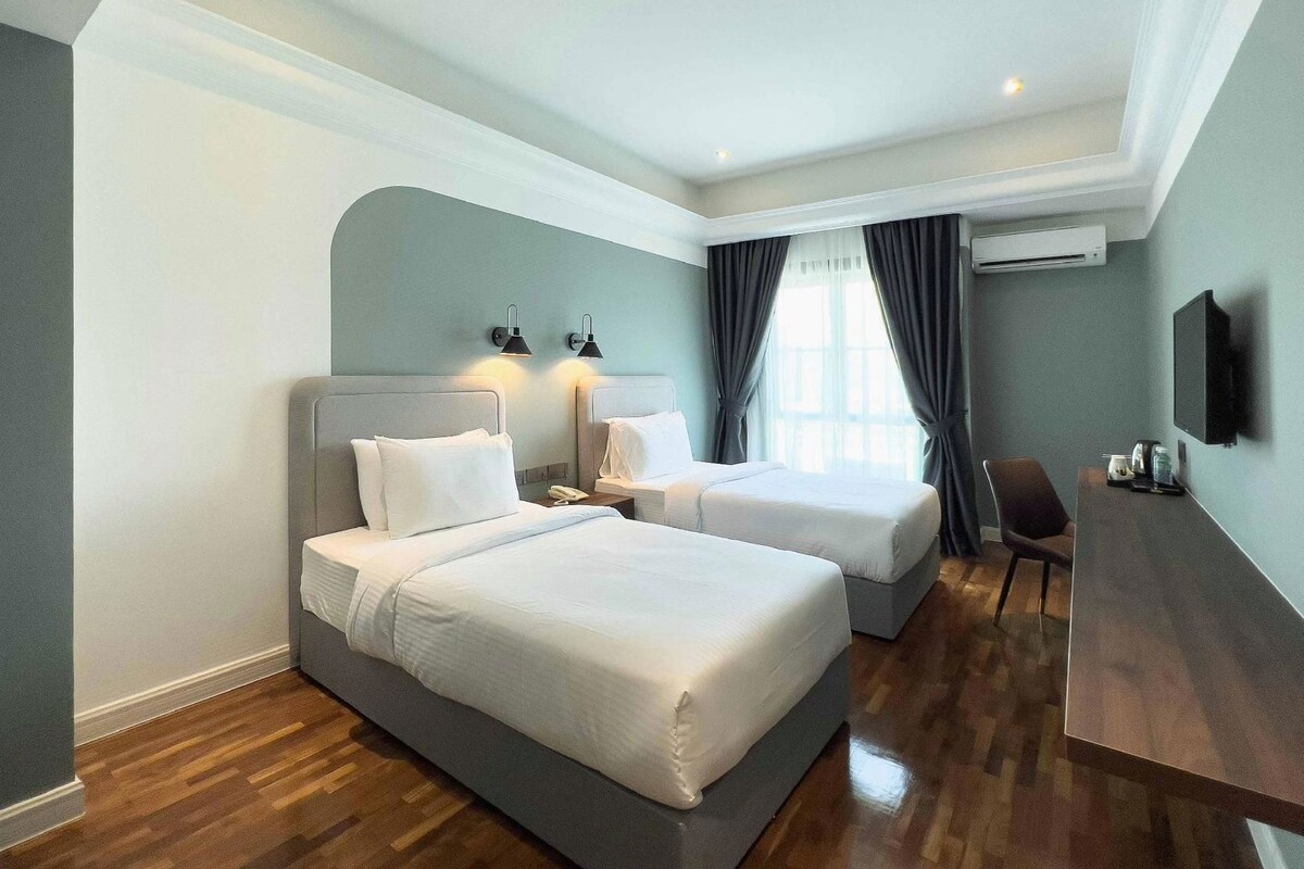 Quarto de hotel com duas camas, uma escrivaninha, uma cadeira e uma televisão.