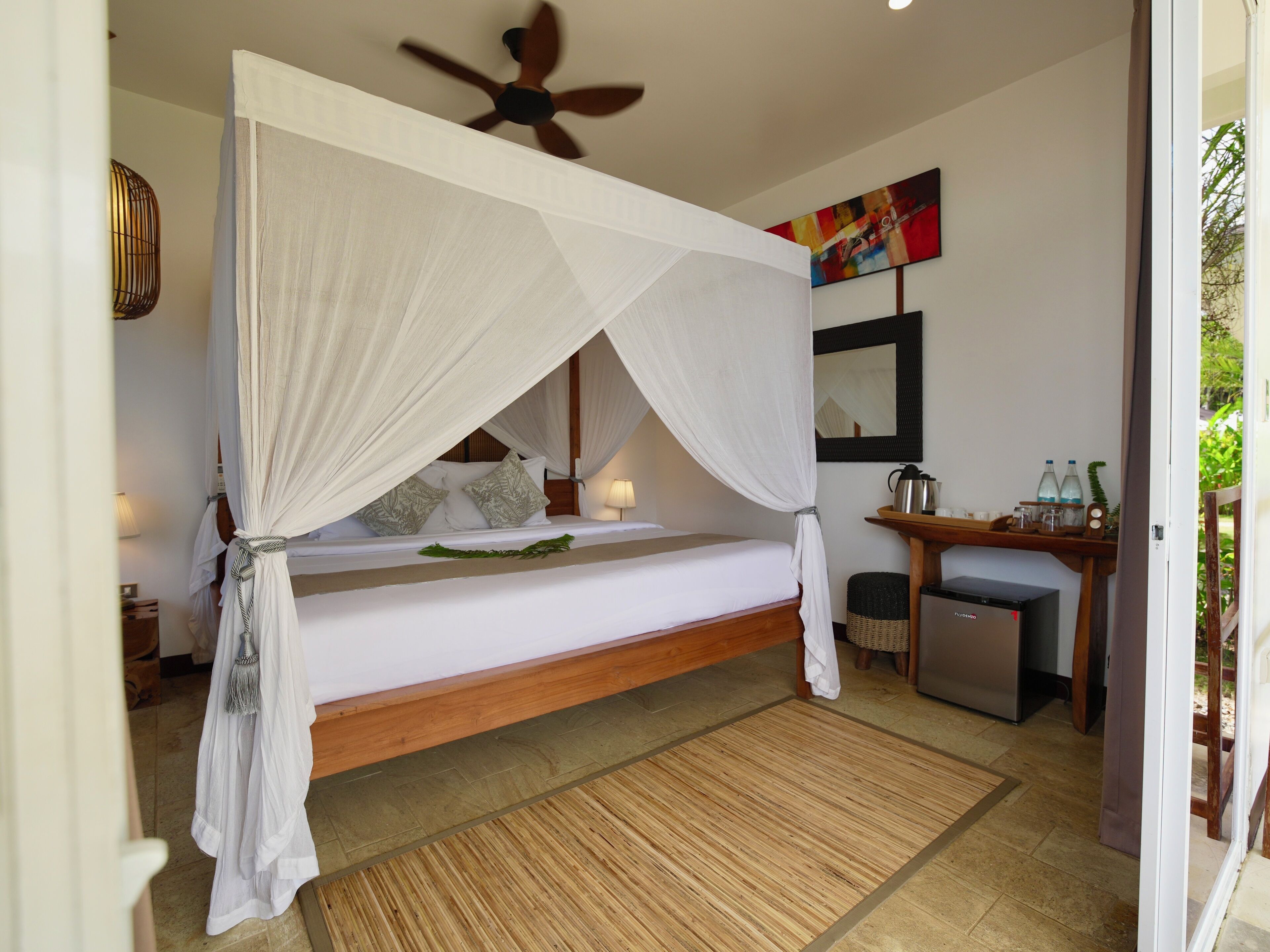 A single bed with a canopy, a ceiling fan, a small table with a kettle, and a mirror on the wall.