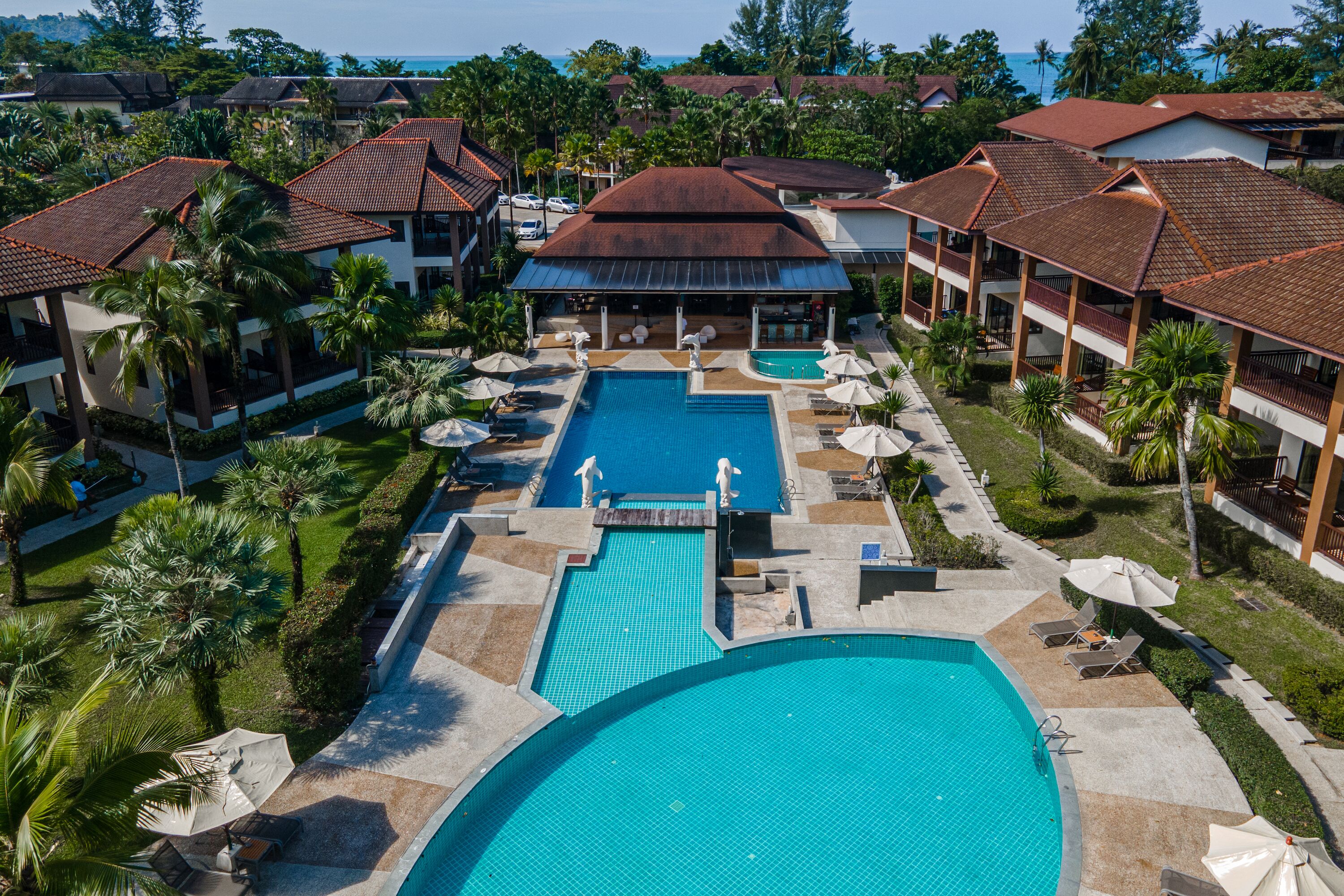 A resort with a central swimming pool, multiple lounge areas, and a view of the ocean.