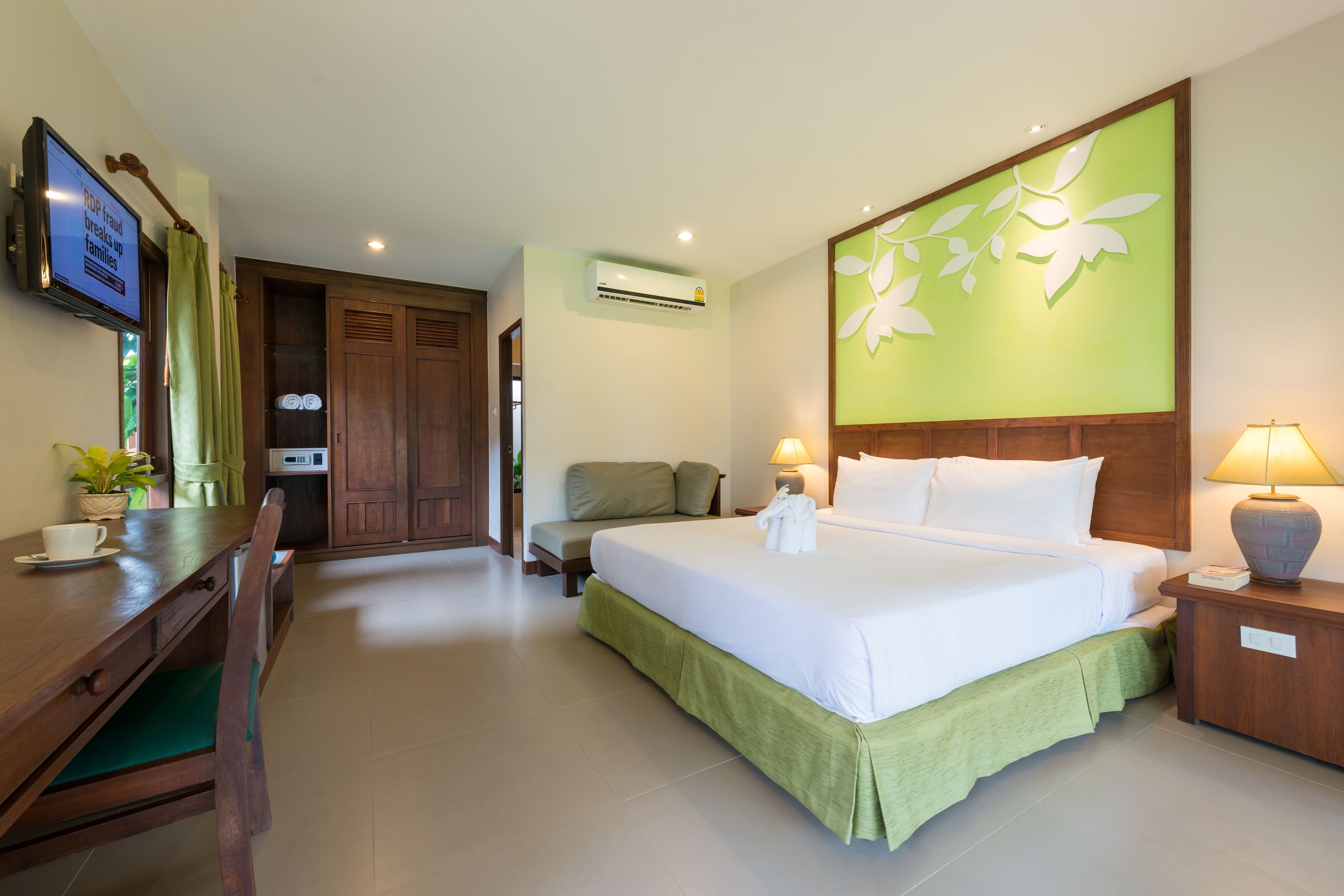 A hotel room with a bed, a desk, a chair, a TV, and an air conditioning unit.