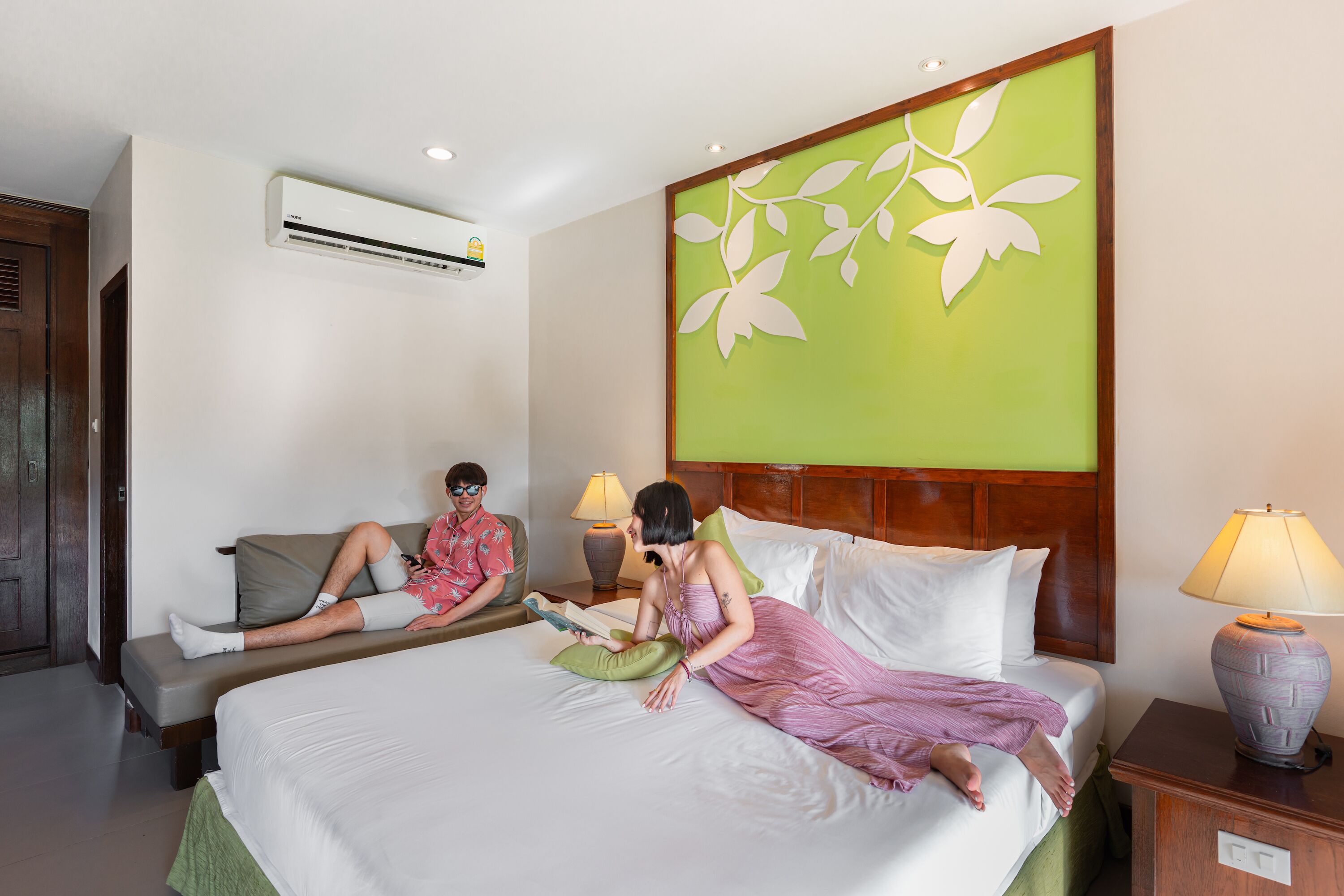 Une chambre d’hôtel avec un lit, un canapé, une table de chevet avec une lampe et un appareil de climatisation fixé au mur.
