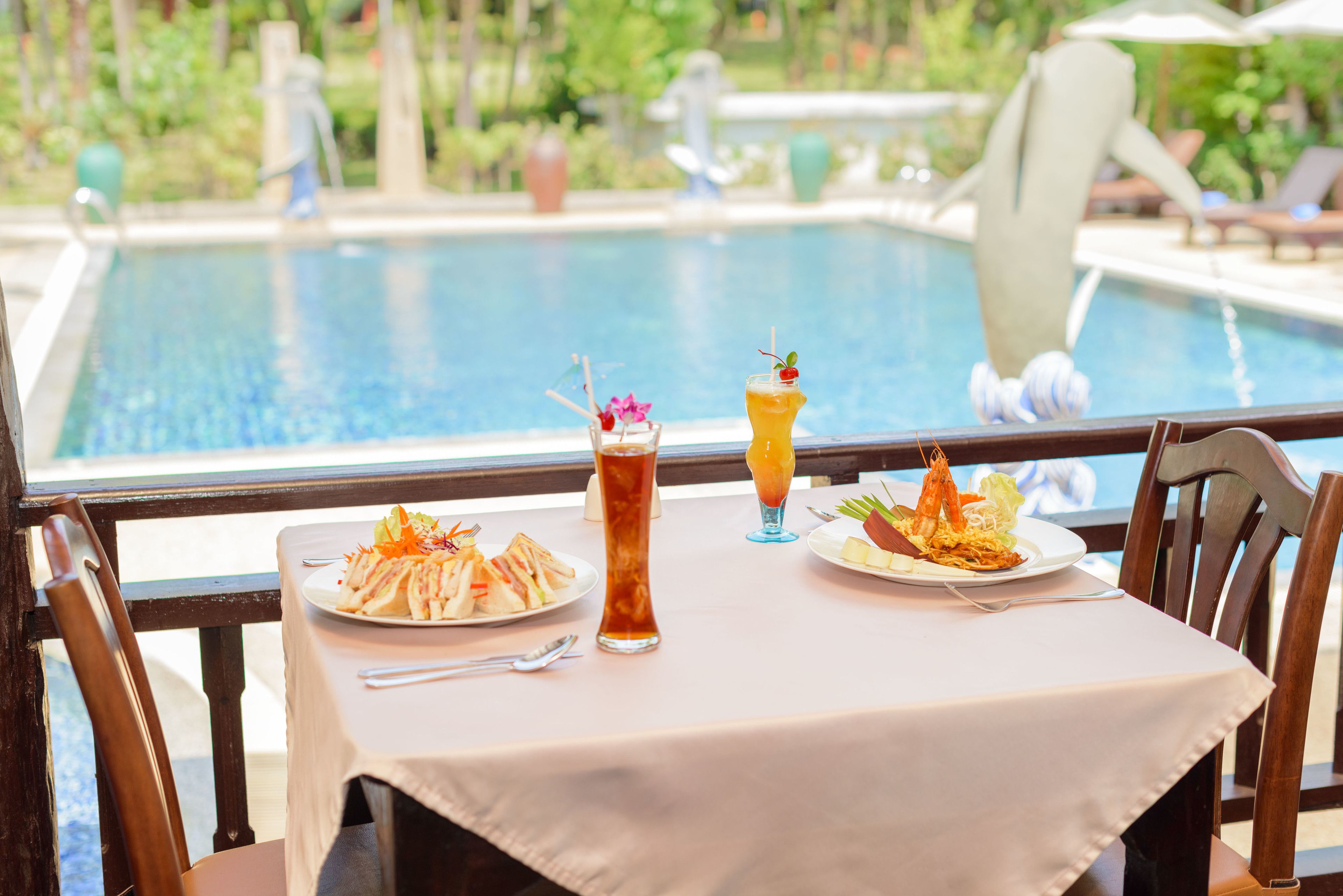 Una mesa de comedor con vista a una piscina, dos platos de comida y dos bebidas.