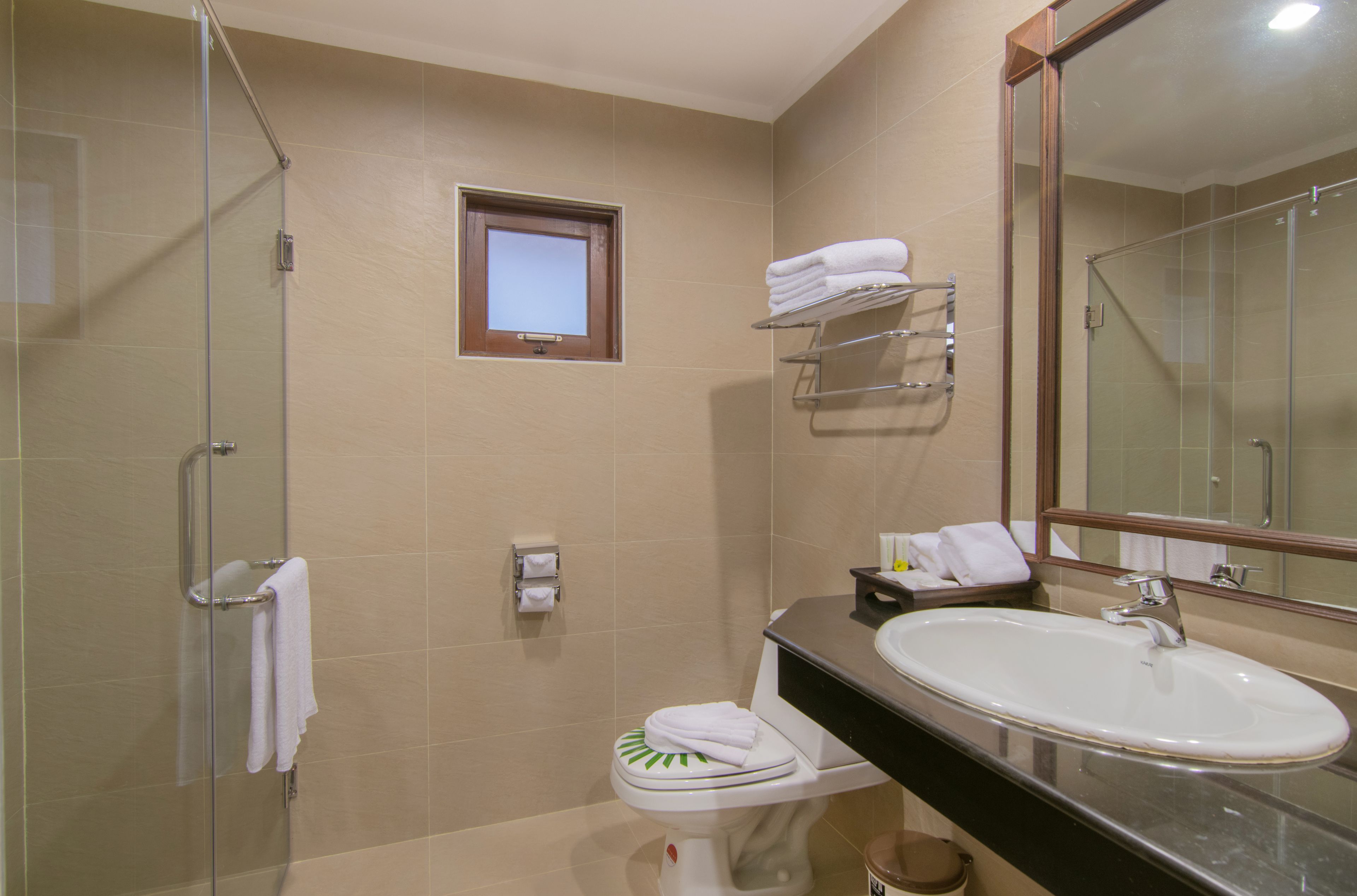 Een moderne badkamer met een douchecabine van glas, een wastafel met spiegel en een klein raam boven het toilet.