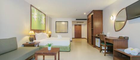 A hotel room with a bed, a sofa, a desk, a chair, a table, a mirror, and a TV.