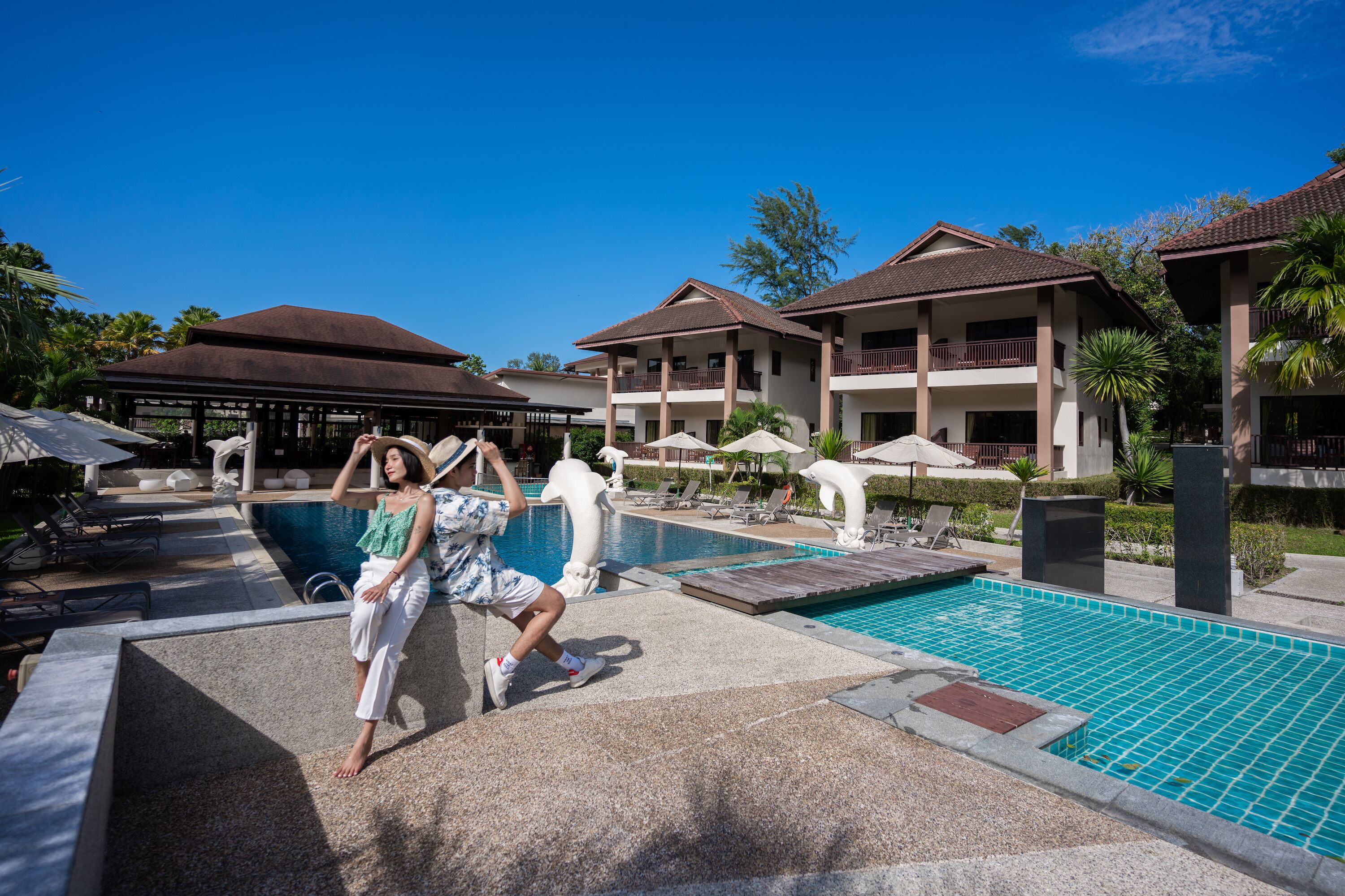 Zona de piscina en un complejo turístico, con sillas de descanso y sombrillas, rodeada de edificios con balcones.