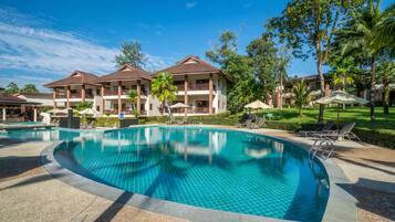 A swimming pool with lounge chairs and umbrellas, surrounded by hotel buildings with balconies and palm trees.