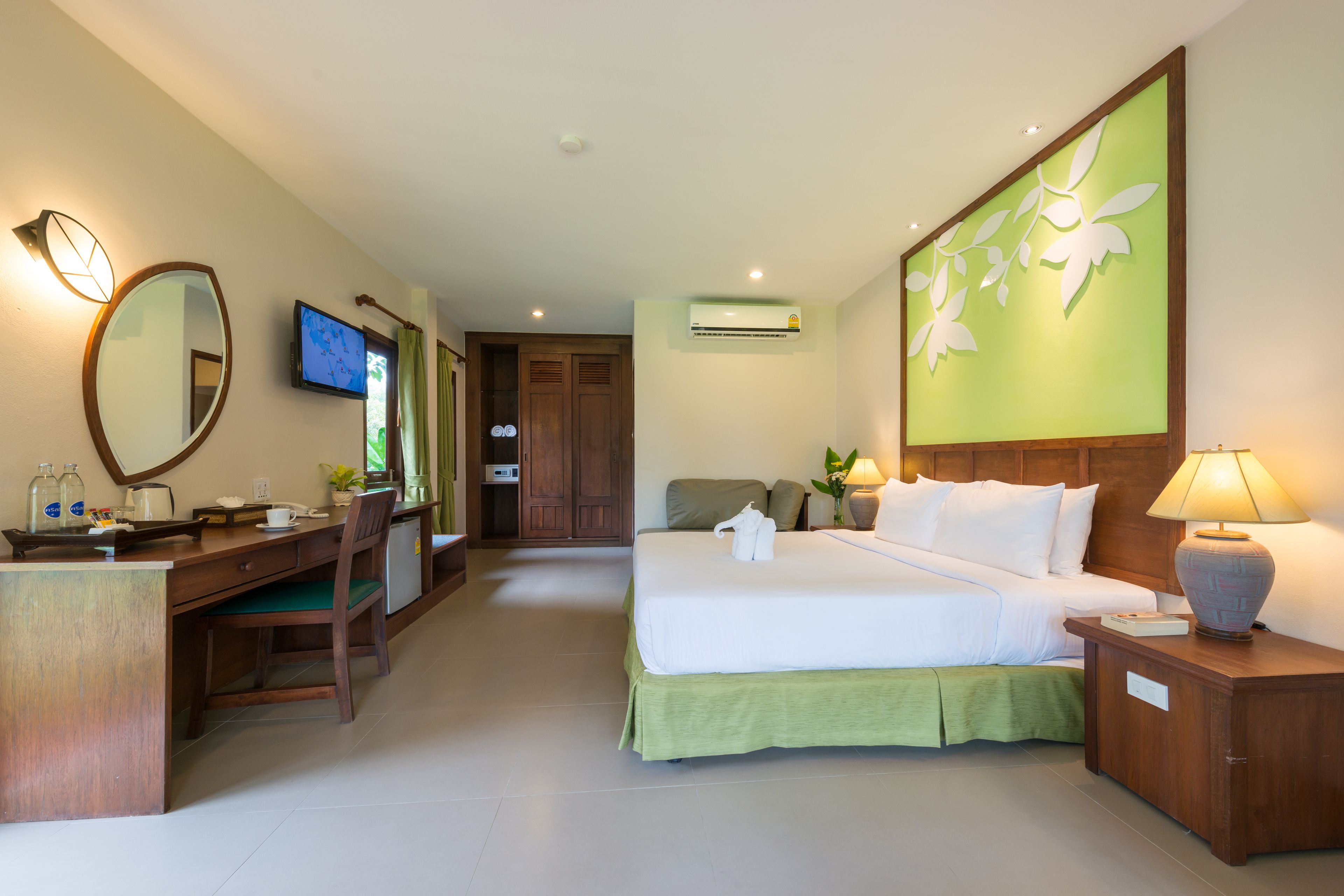 A hotel room with a bed, desk, chair, TV, and a wall-mounted air conditioner.