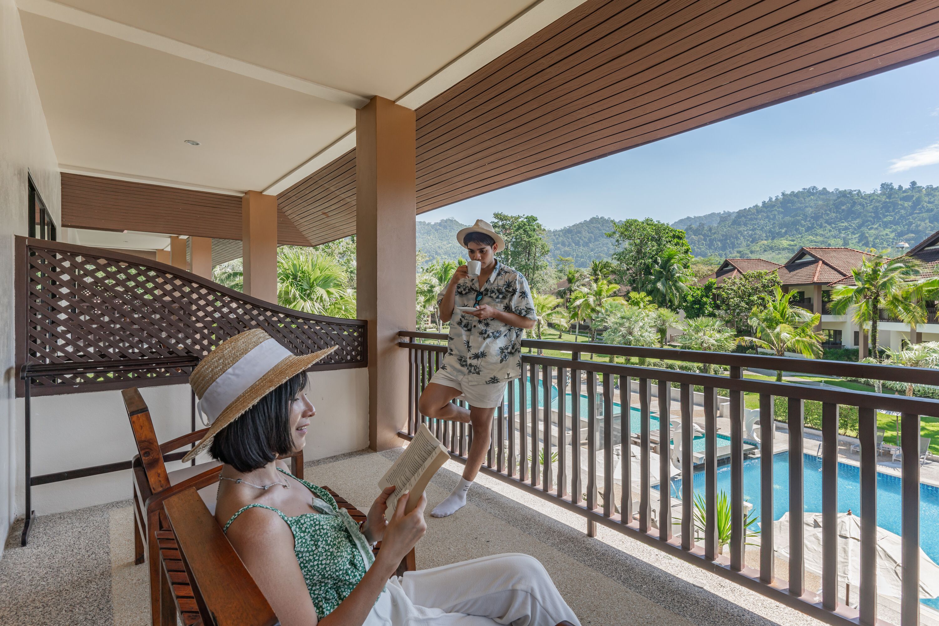 A balcony with a pool view, wooden furniture, and a person reading a book.