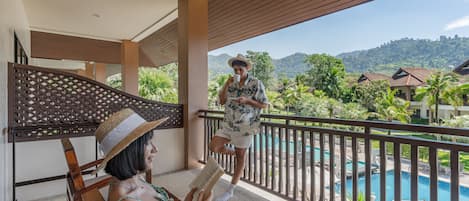 A balcony with a pool view, wooden furniture, and a person reading a book.