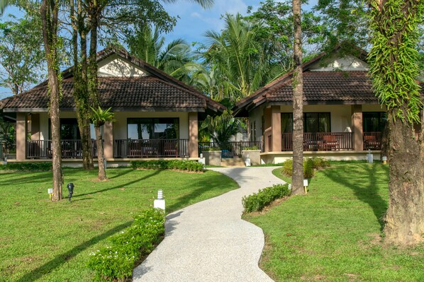 Un sendero conduce a dos edificios tipo bungalow con balcones, rodeados de exuberante vegetación y palmeras.