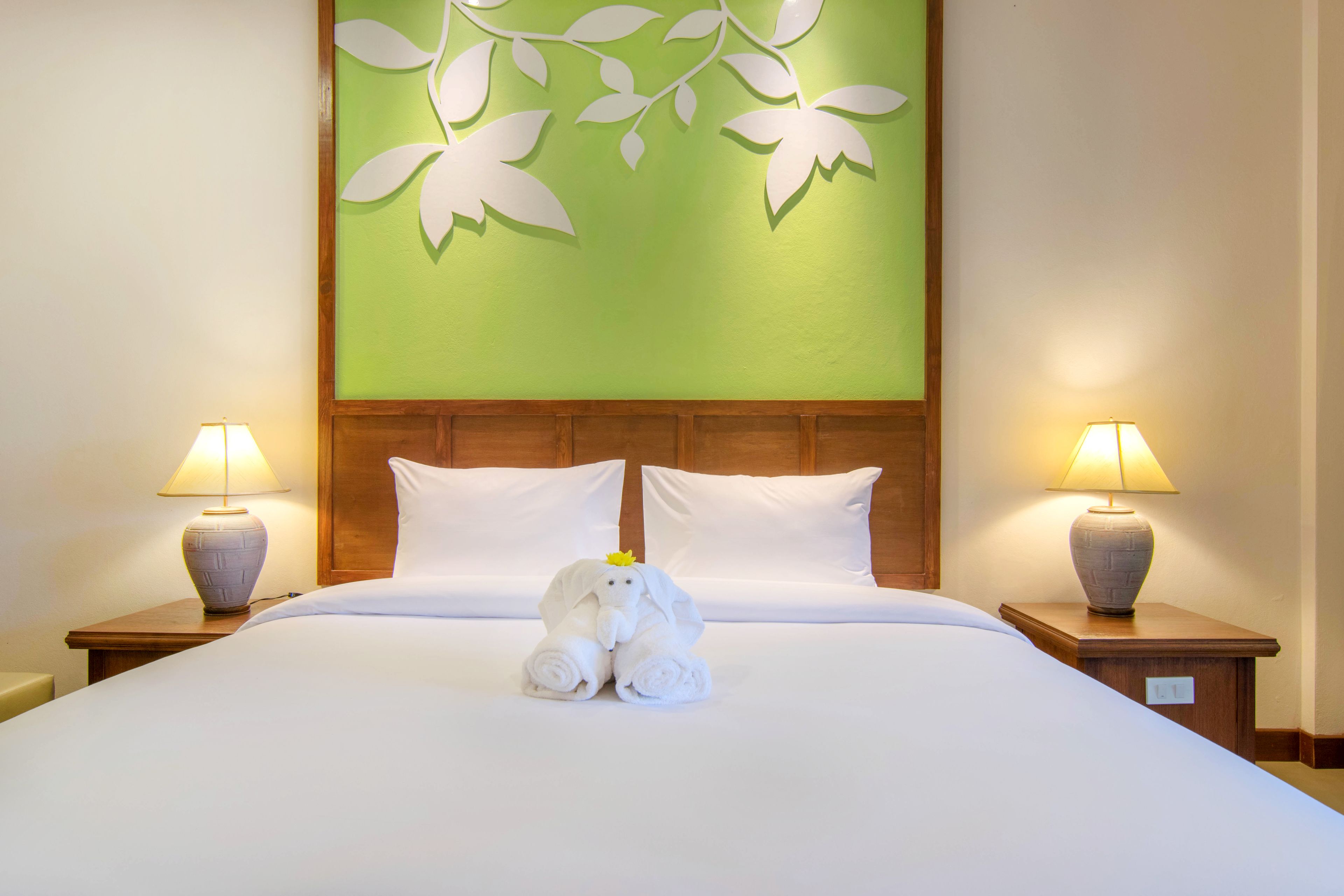 A hotel room with a neatly made bed, two bedside lamps, and a decorative wall panel.