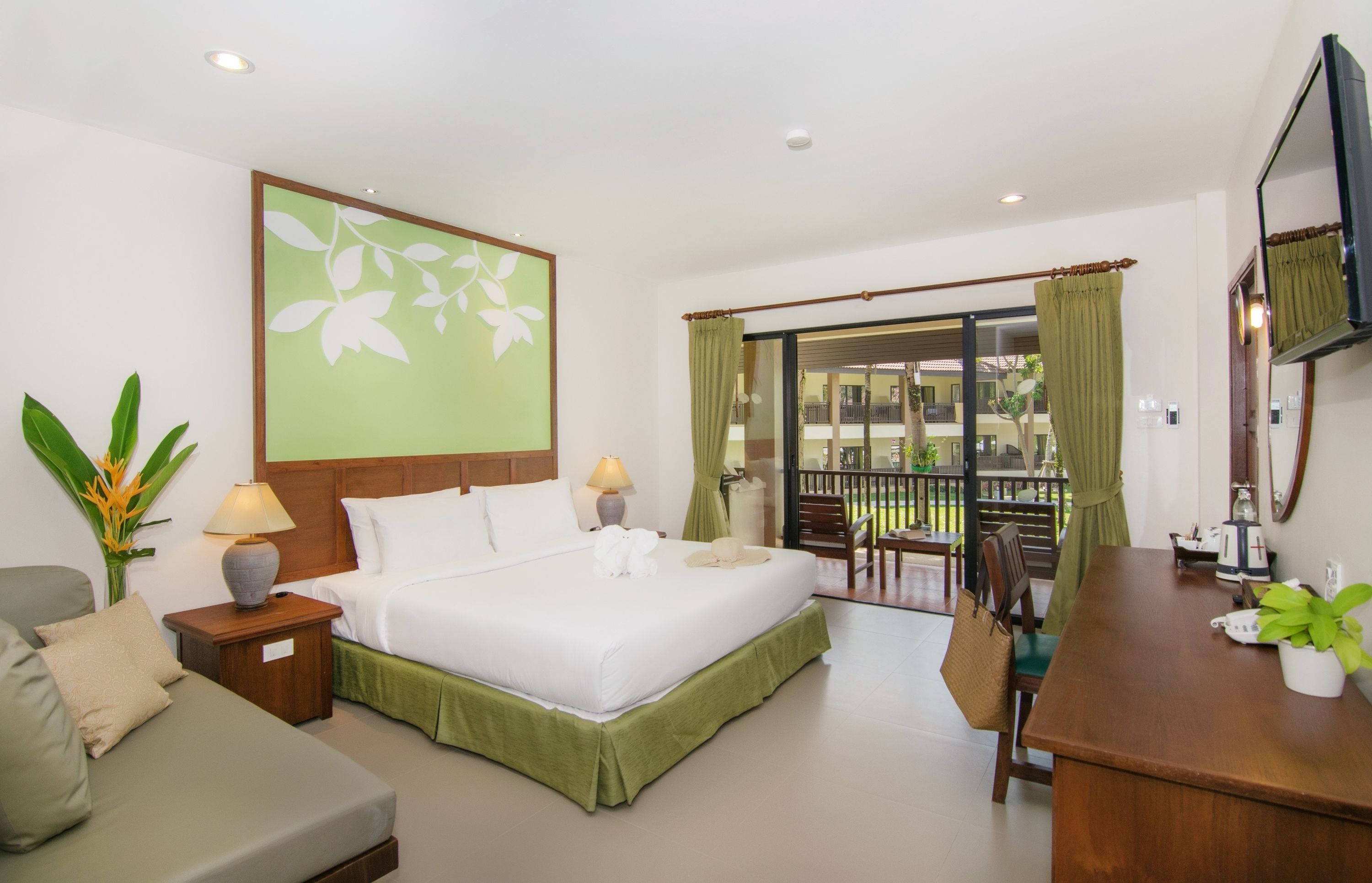 A hotel room with a bed, a desk, a chair, a TV, and a balcony with a view.