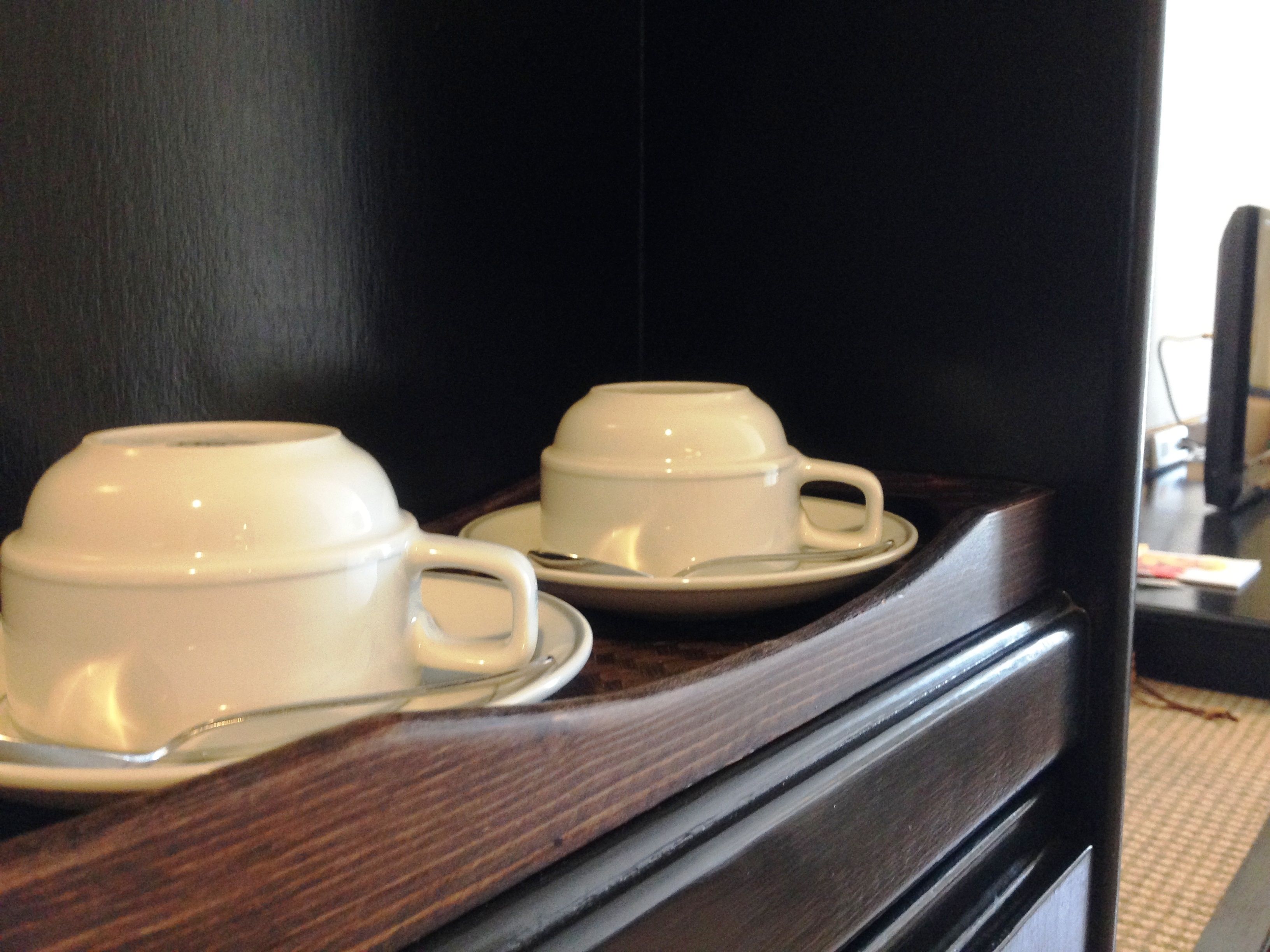 Deux tasses blanches, accompagnées de leurs soucoupes, sont posées sur une surface en bois sombre, probablement une table d’appoint dans une chambre d’hôtel.
