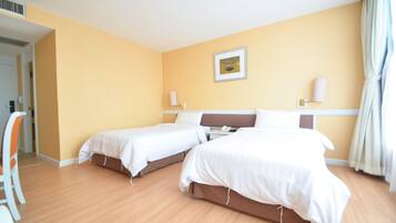 A hotel room with two single beds, a bedside table with a lamp, a framed picture on the wall, and a window with curtains.