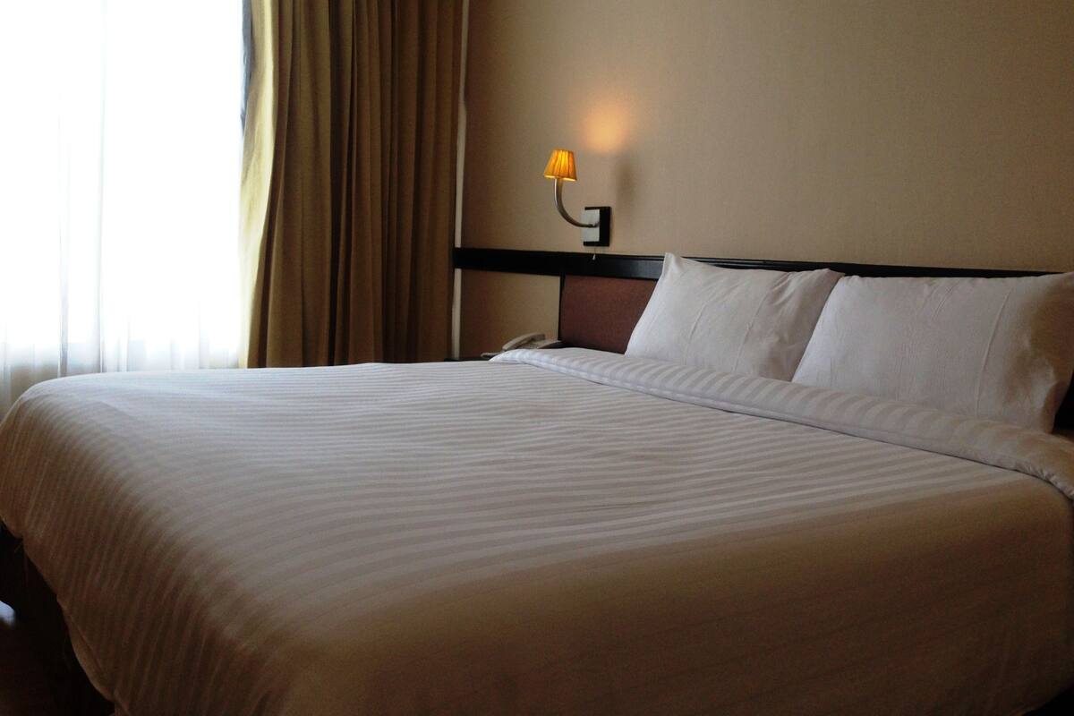 Une chambre d’hôtel avec un grand lit, une table de chevet, une lampe et une fenêtre avec des rideaux.