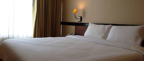 Quarto de hotel com uma cama grande, uma mesa de cabeceira, um abajur e uma janela com cortinas.