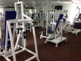 Un gimnasio con diversas máquinas de ejercicio, suelo alfombrado y espejos en las paredes.
