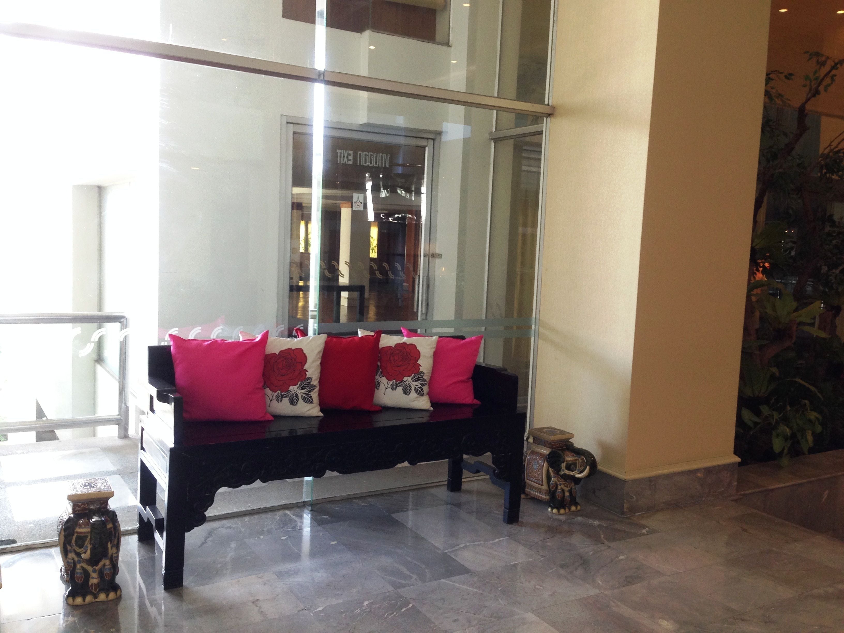 A black bench with pink and white cushions, a glass wall, and a decorative elephant statue.