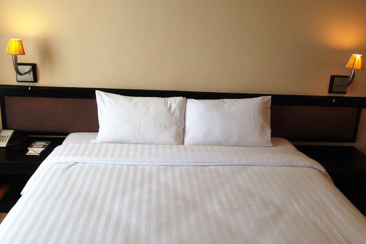 Une chambre d’hôtel avec un lit bien fait, deux lampes de chevet, une table de chevet avec un téléphone et un tableau encadré.