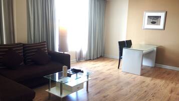A living room with a sofa, a glass coffee table, a desk, and a chair.