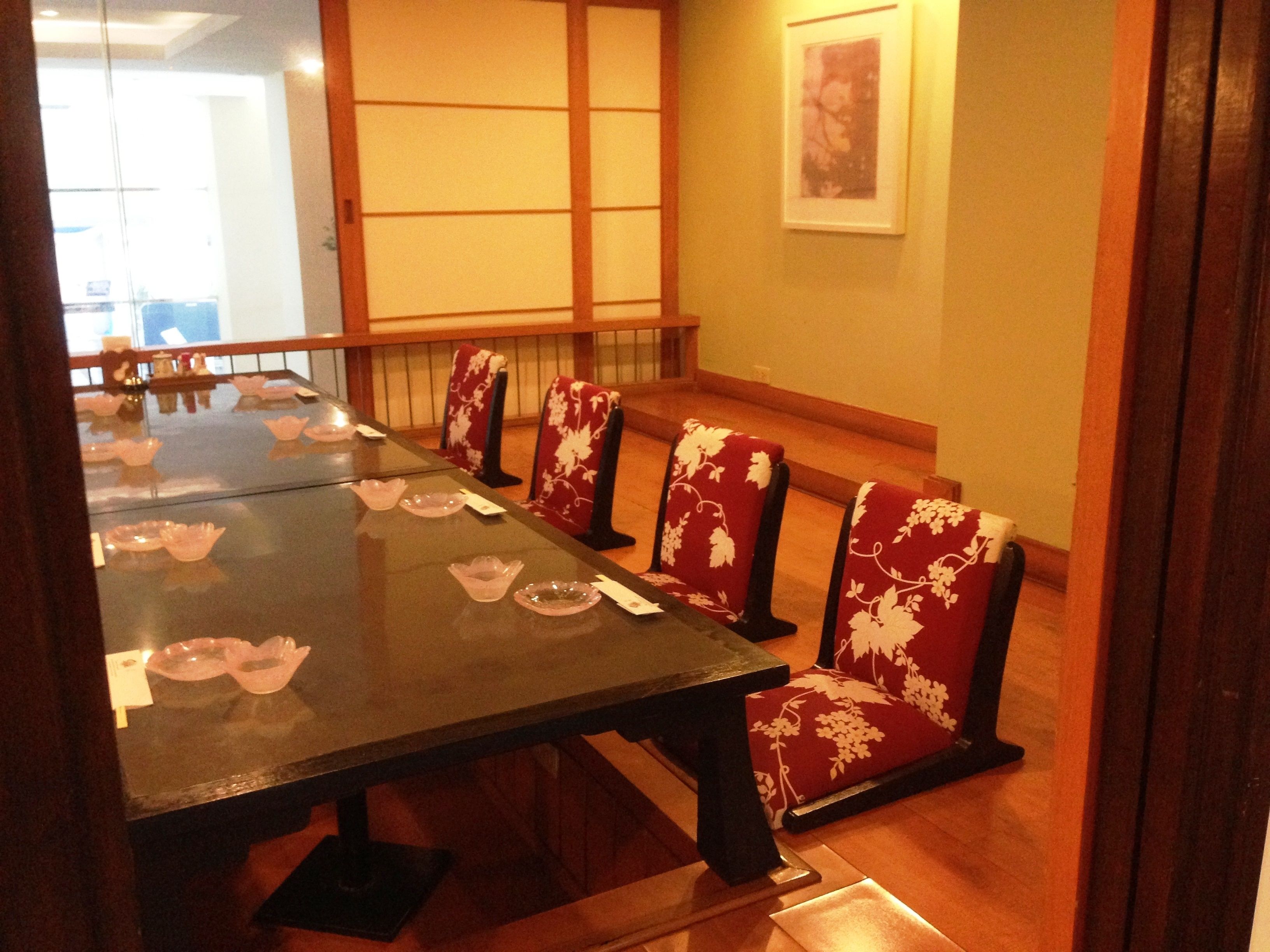 Une salle à manger de style japonais traditionnel, avec une longue table et des chaises à motifs floraux rouges.