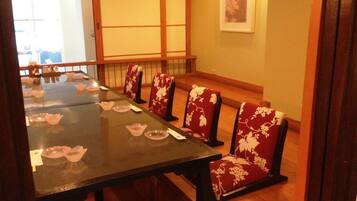 Une salle à manger de style japonais traditionnel, avec une longue table et des chaises à motifs floraux rouges.