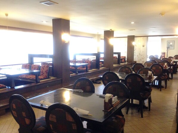 Un restaurante con mesas, cabinas y ventanas amplias, y piso de baldosas.