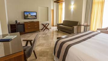 Habitación de hotel con cama, sofá, escritorio con computadora, televisión y una mesita.