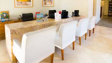 A reception area with a marble counter, white cushioned chairs, framed pictures on the wall, and a staircase in the background.