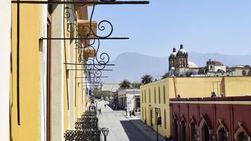 A street with yellow buildings, a bell tower, and mountains in the background.