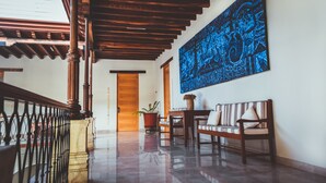 A spacious hallway with a wooden staircase, a large blue artwork on the wall, a bench, and a potted plant. - Hotel Parador de Alcalá Oaxaca (Oaxaca)