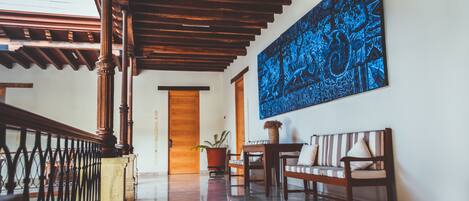 A spacious hallway with a wooden staircase, a large blue artwork on the wall, a bench, and a potted plant.