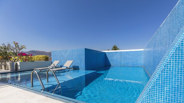 A clear blue swimming pool with a tiled edge, a lounge area with chairs, and a view of distant mountains. - Hotel Parador de Alcalá Oaxaca (Oaxaca)