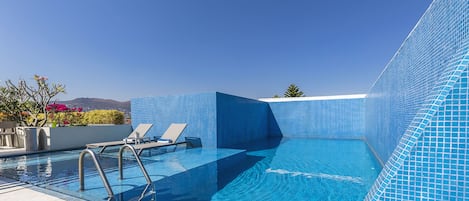 Una piscina al aire libre, sombrillas, sillones reclinables de piscina