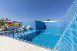 Ein klarer, blauer Swimmingpool mit einer gefliesten Kante, eine Lounge-Bereich mit Stühlen und Blick auf entfernte Berge.