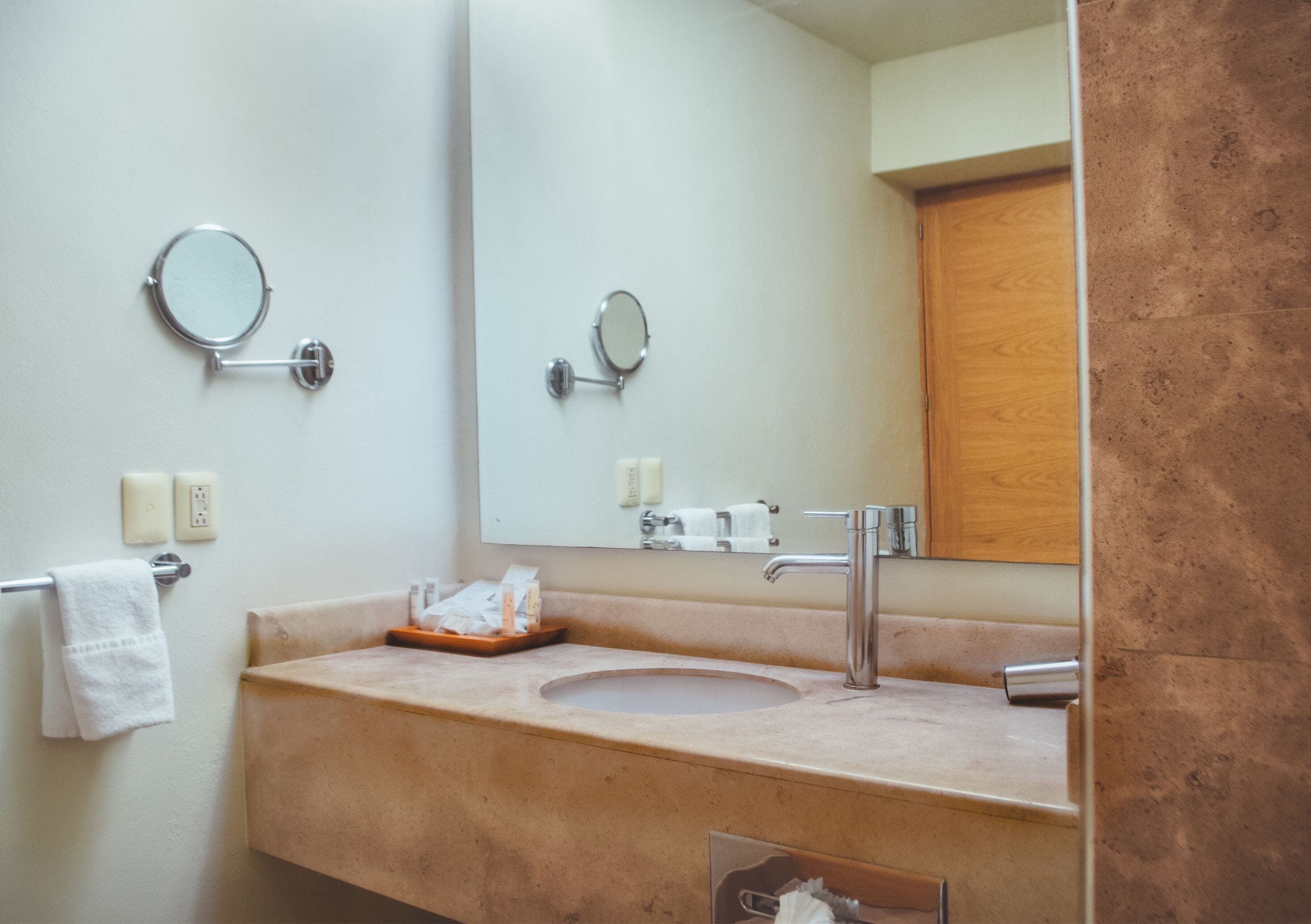 A bathroom with a sink, mirror, towel rack, and a wooden door.