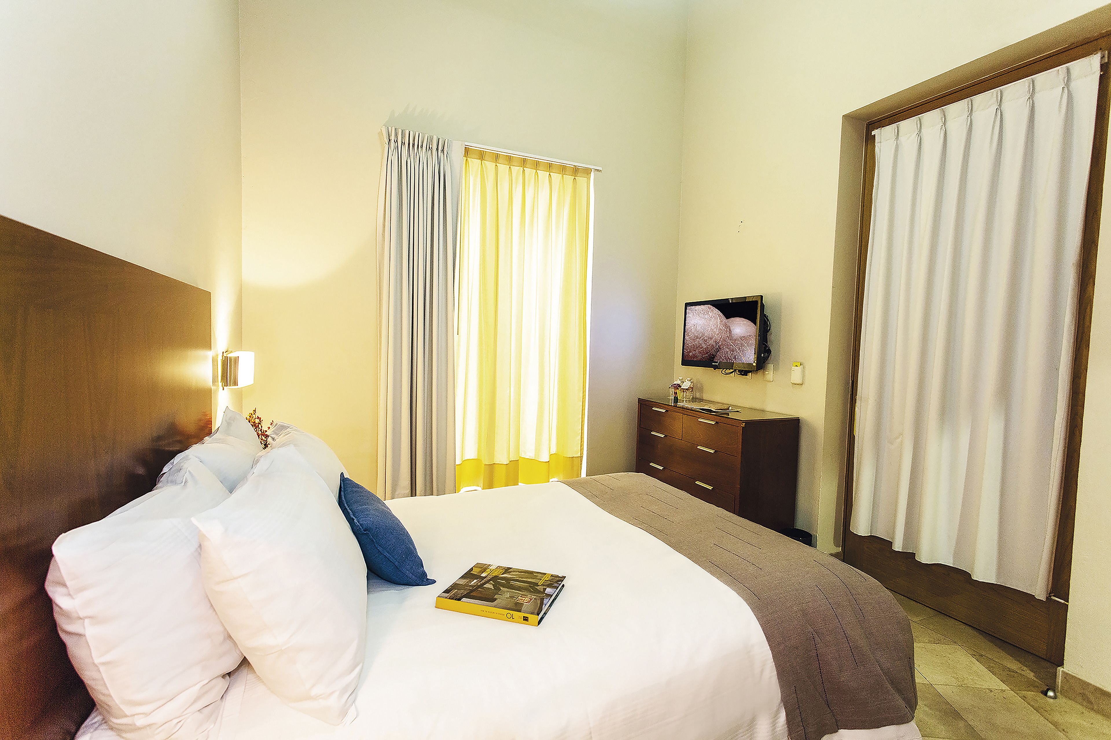 Una camera d'albergo con un letto, una televisione, un comò e una finestra con tende.