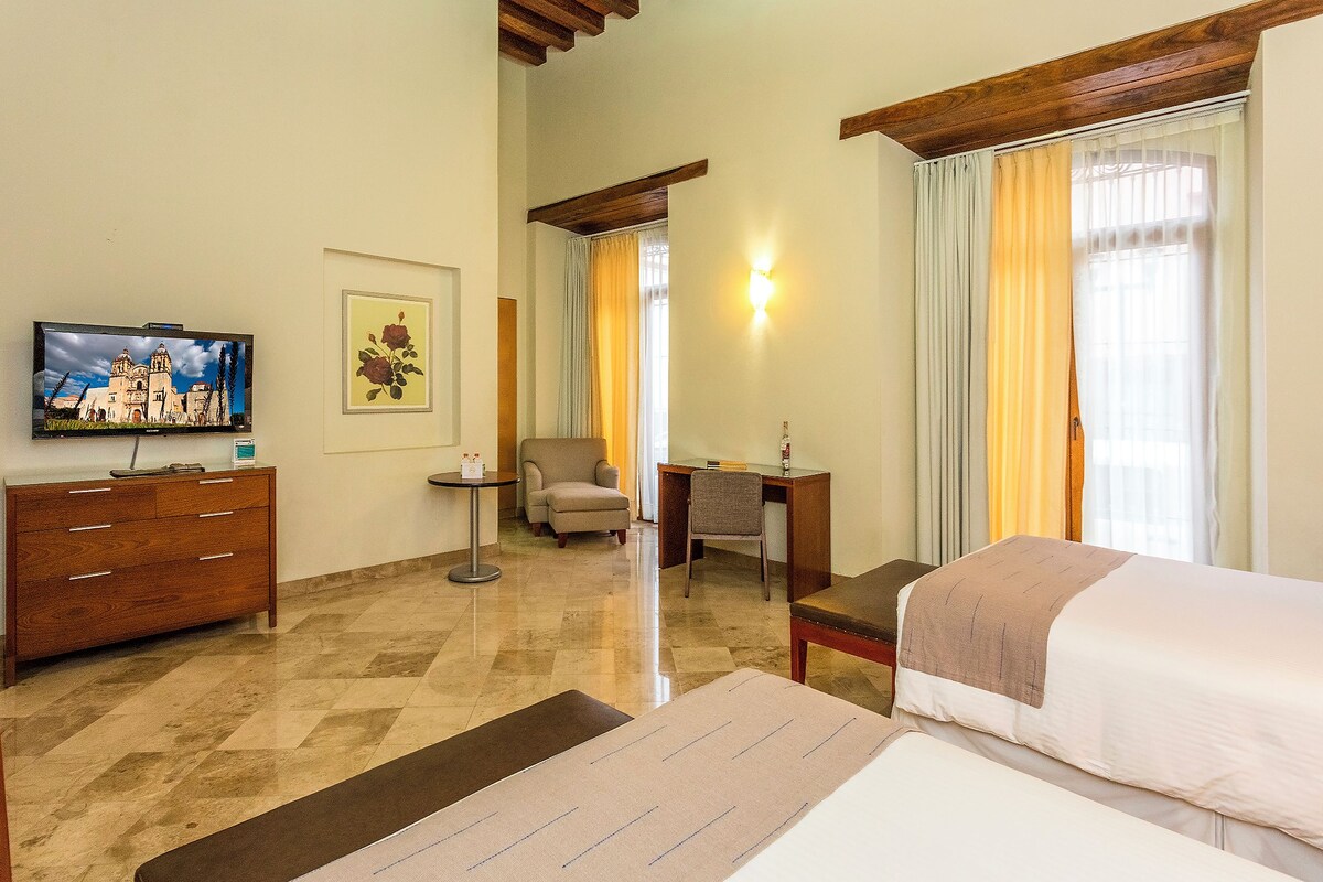 Una habitación de hotel con una cama, un escritorio, una silla, un televisor y un cuadro en la pared.