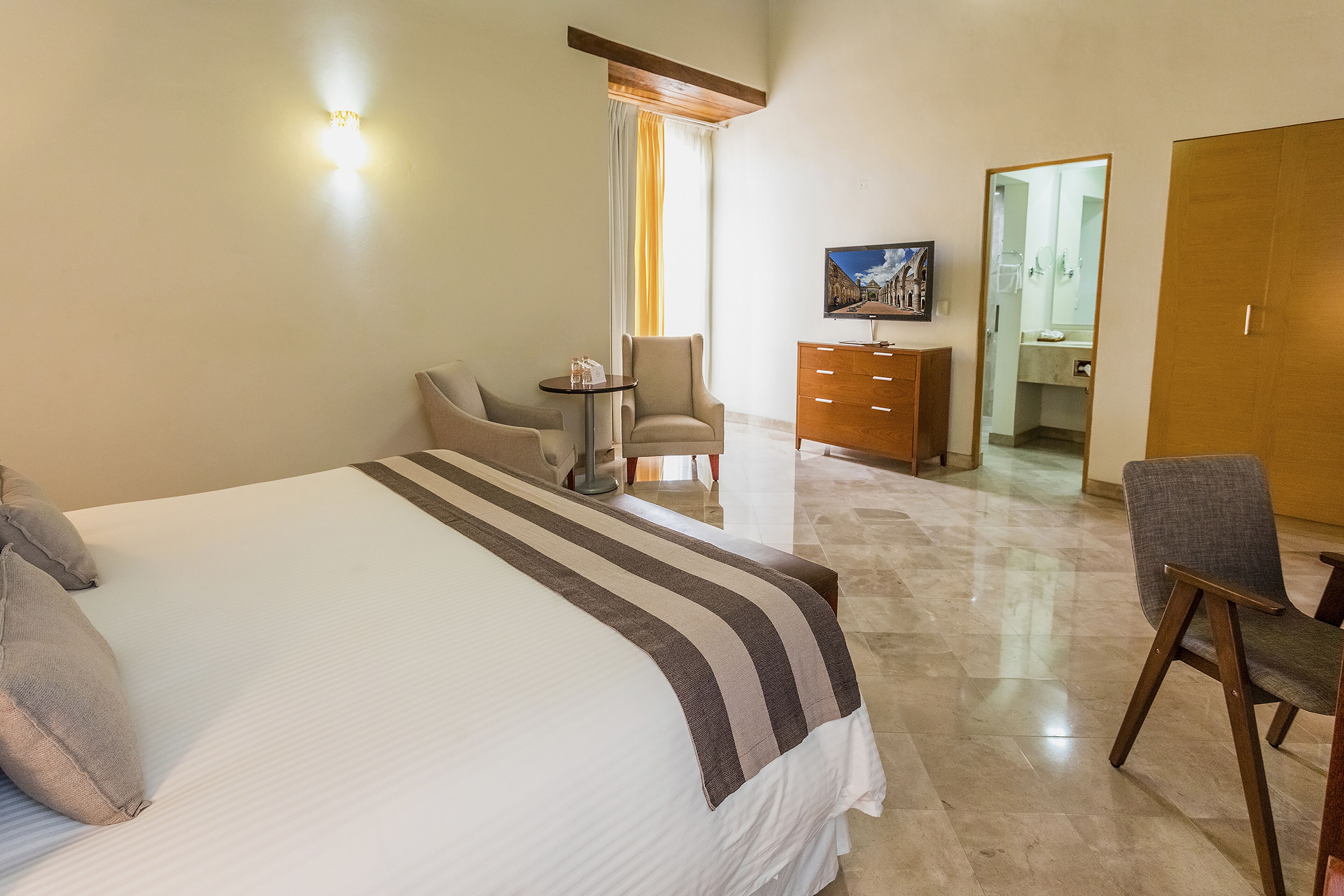 Een hotelkamer met een groot bed, een stoel, een klein tafeltje, een dressoir en een televisie.