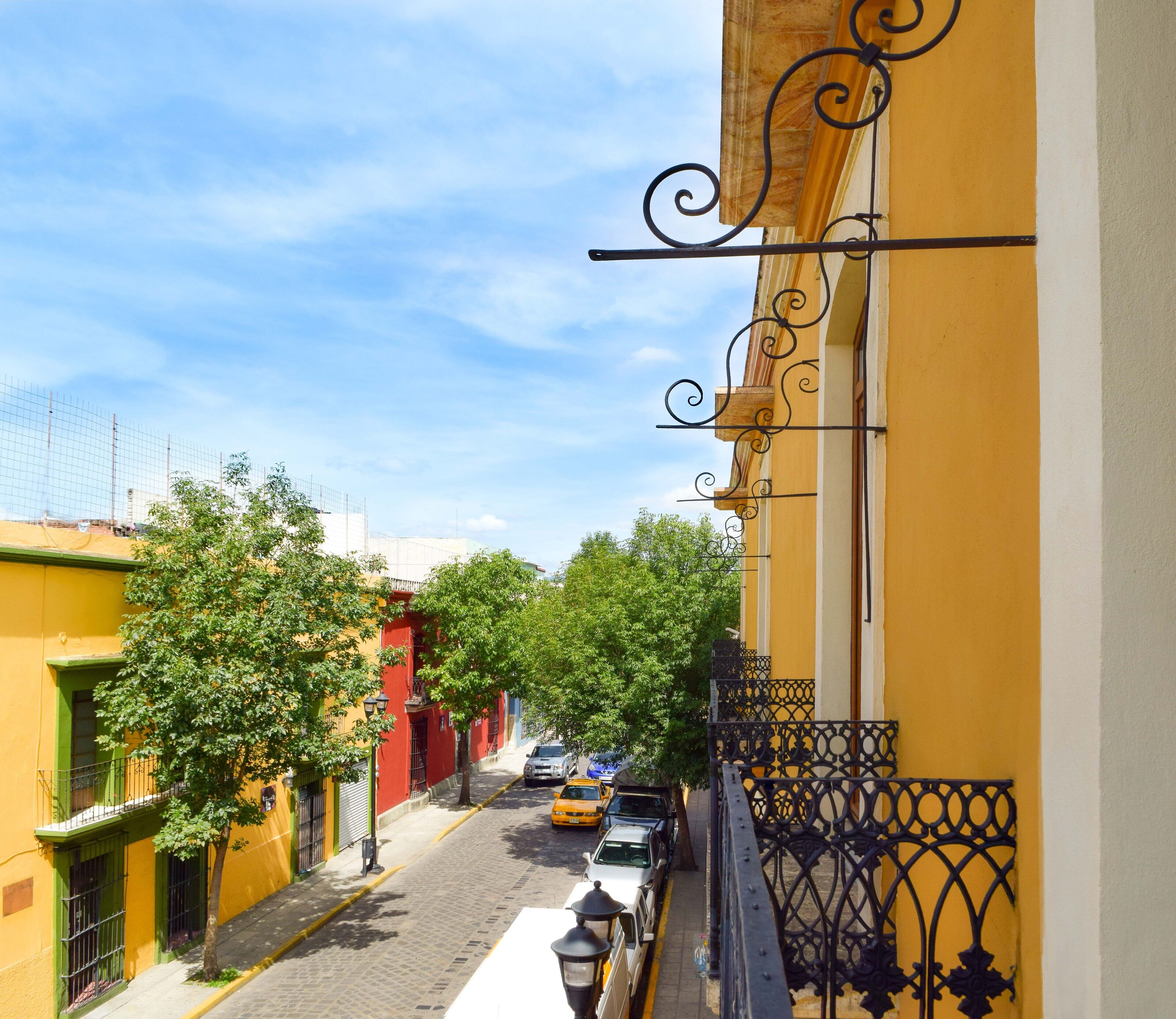 A narrow street with yellow buildings, trees, and parked cars.