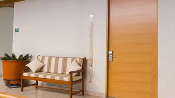 Una puerta de madera con manija metálica, un sofá beige con cojines a rayas y una planta en maceta junto al sofá.