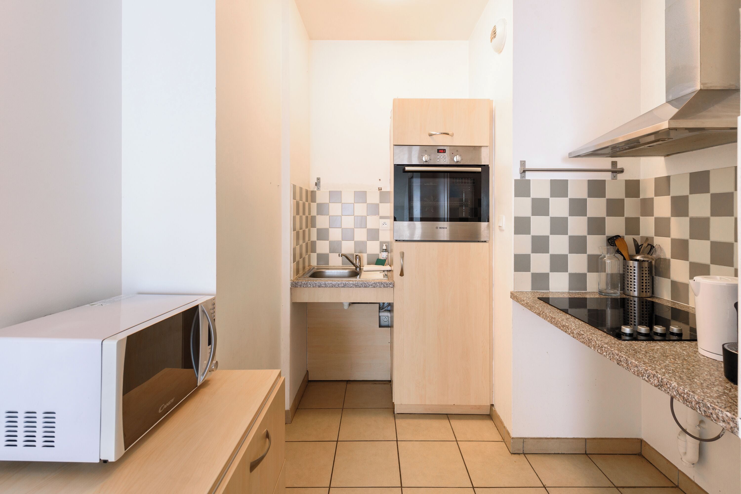 A compact kitchen with a microwave, oven, and a checkered backsplash.