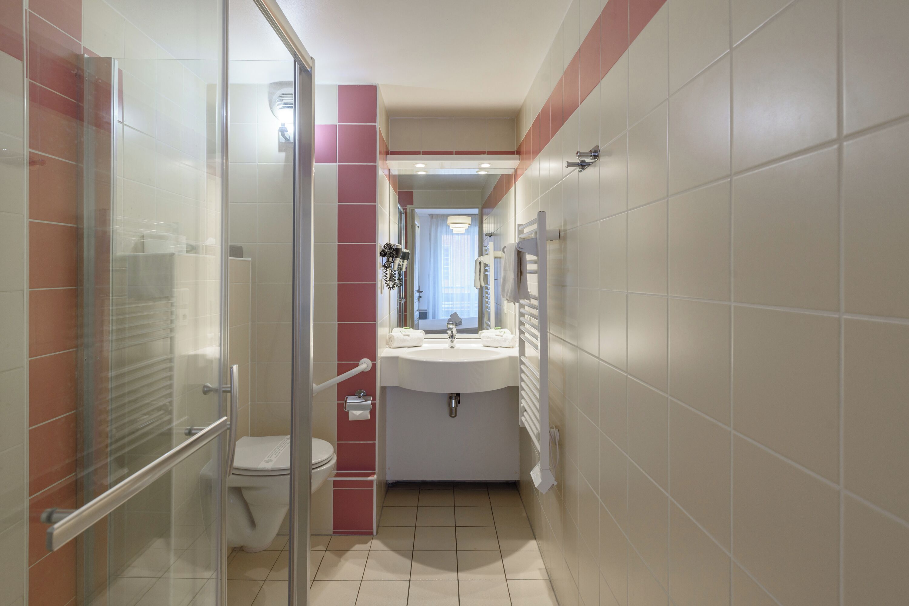 A bathroom with a glass shower enclosure, a toilet, a sink, and a mirror.