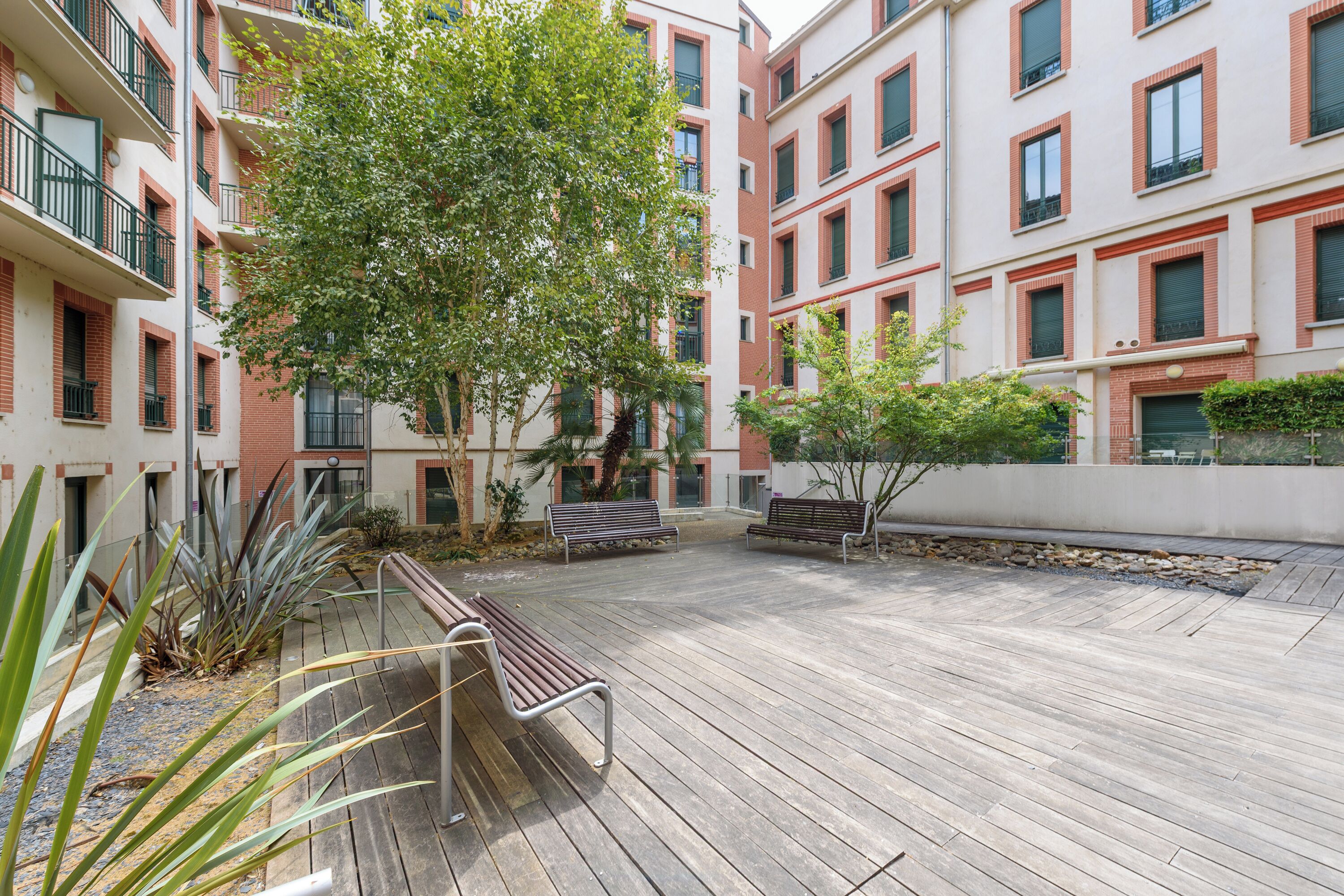 Une cour avec des bancs en bois, un arbre et un bâtiment doté de balcons.