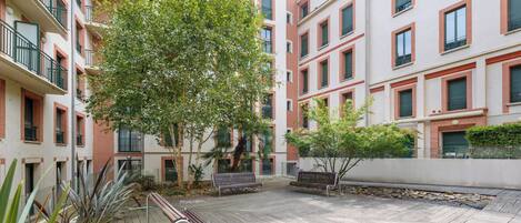 Une cour avec des bancs en bois, un arbre et un bâtiment doté de balcons.