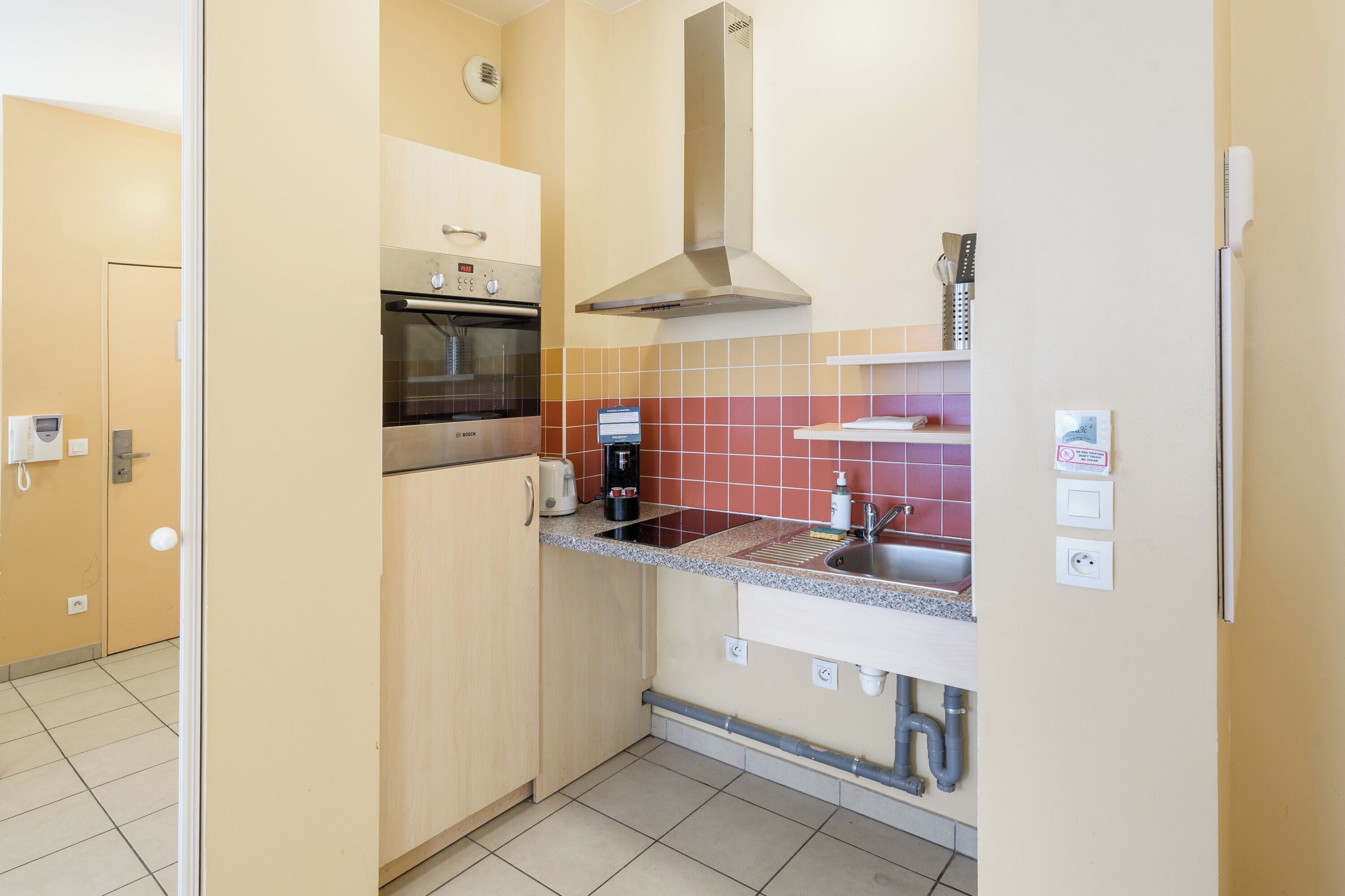 A compact kitchen with a built-in oven, a coffee maker, and a stainless steel range hood.