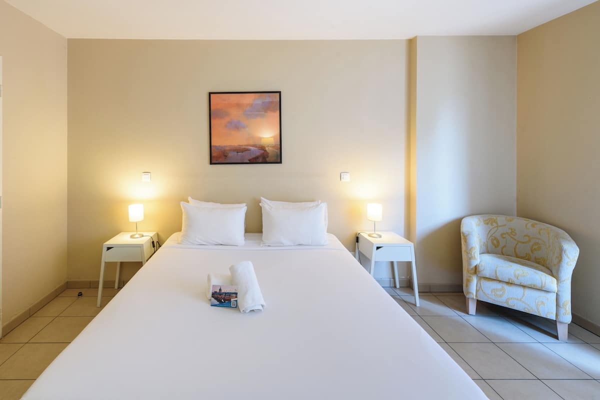Habitación de hotel con una cama grande, dos mesitas de noche con lámparas, una silla y un cuadro en la pared.