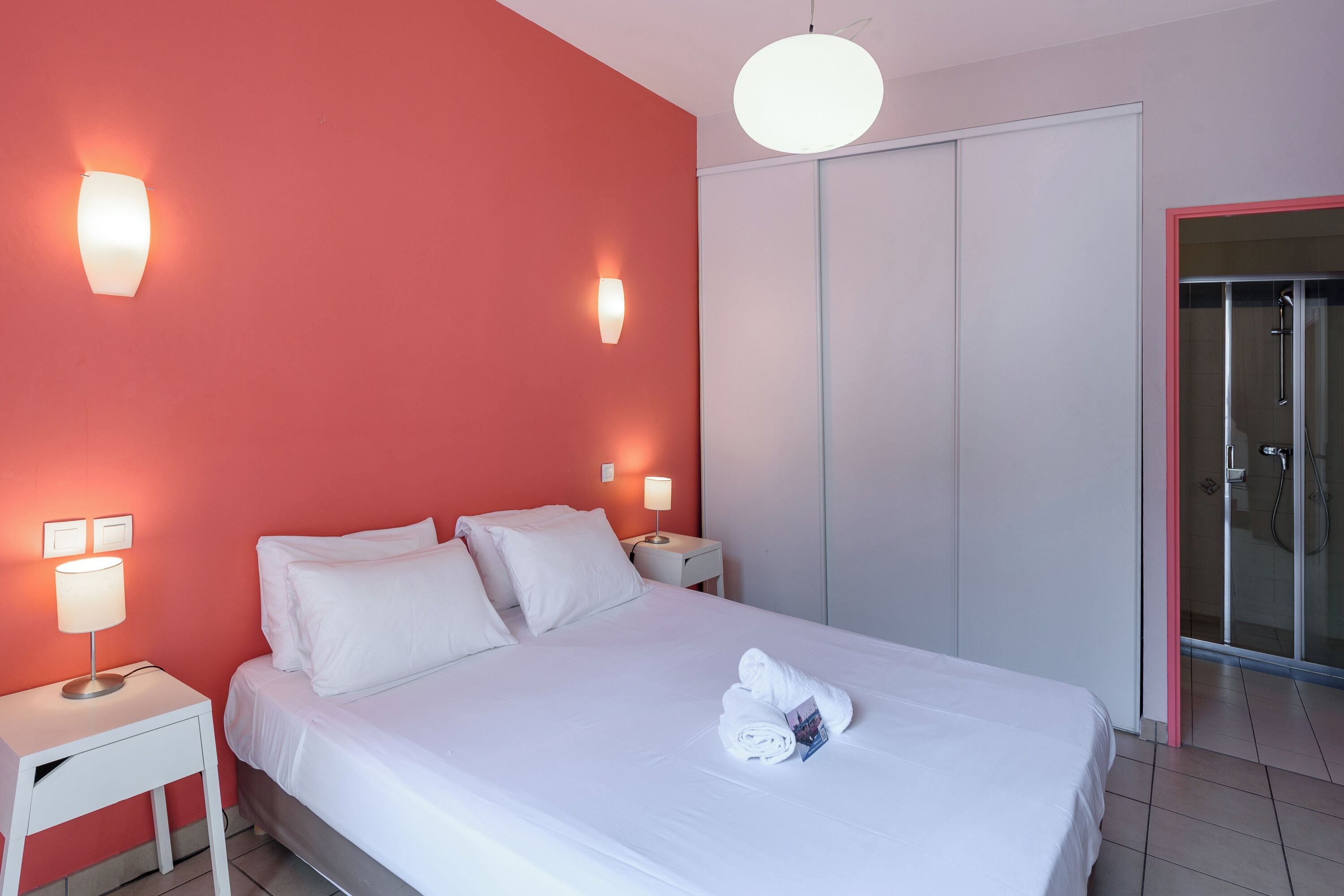 Un lit bien fait, avec des draps blancs, deux lampes de chevet et une serviette posée sur le lit.