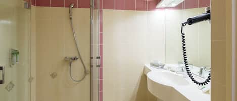 Un baño con cabina de ducha de vidrio, un lavamanos blanco y un espejo.