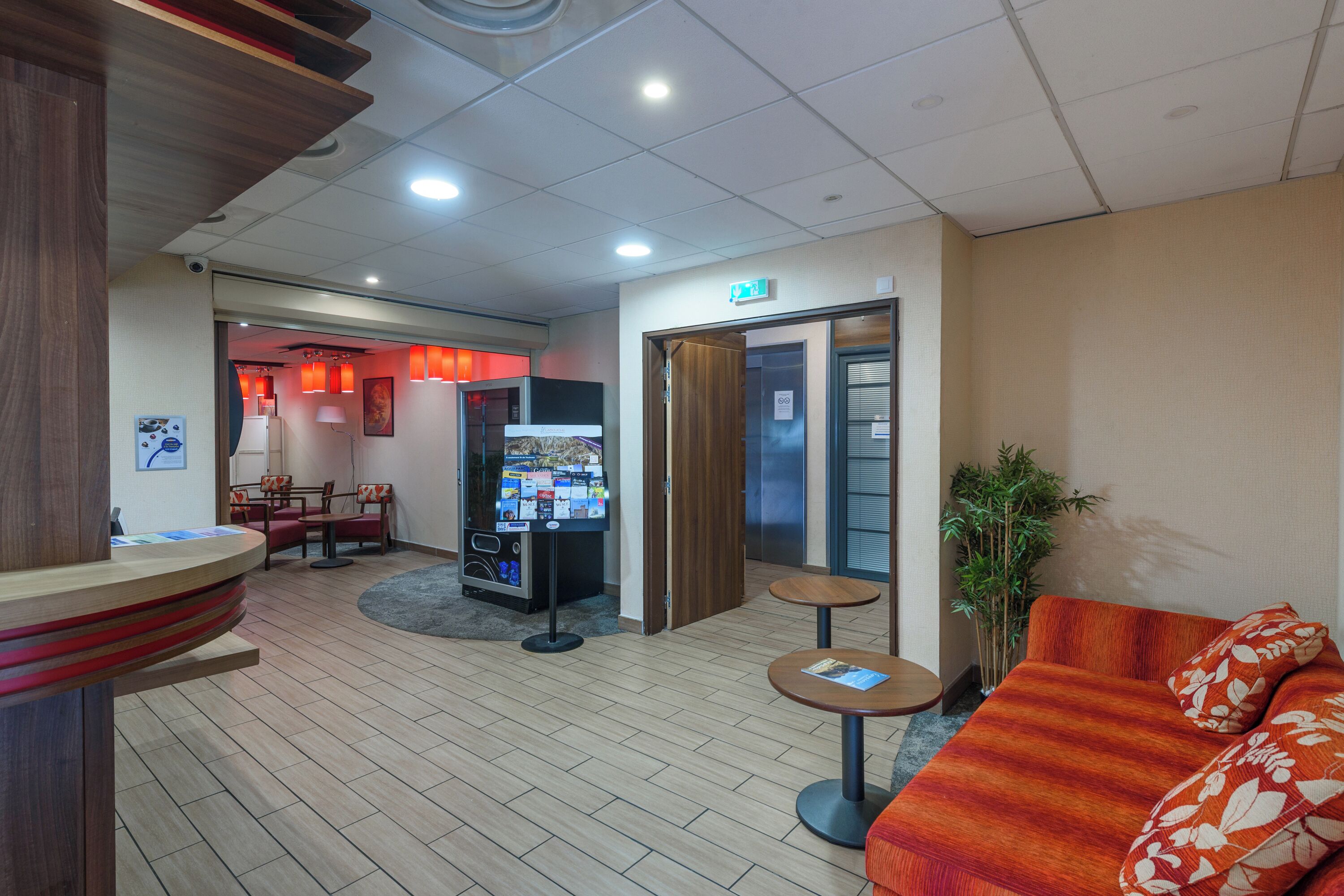 A lobby with a reception desk, seating area, vending machine, and an elevator.